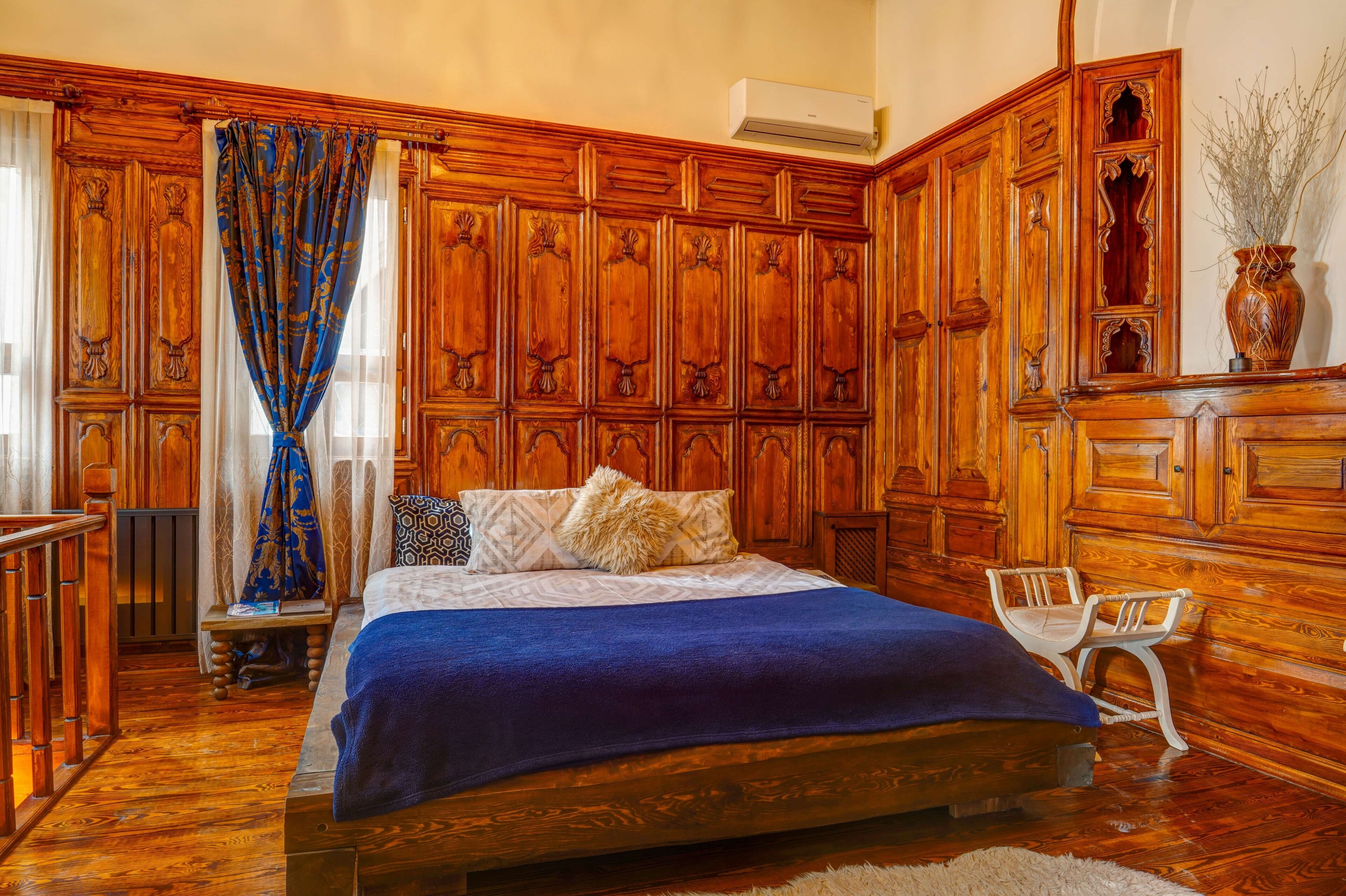 Een slaapkamer met een houten bed, een bankje, een stoel en een dressoir.