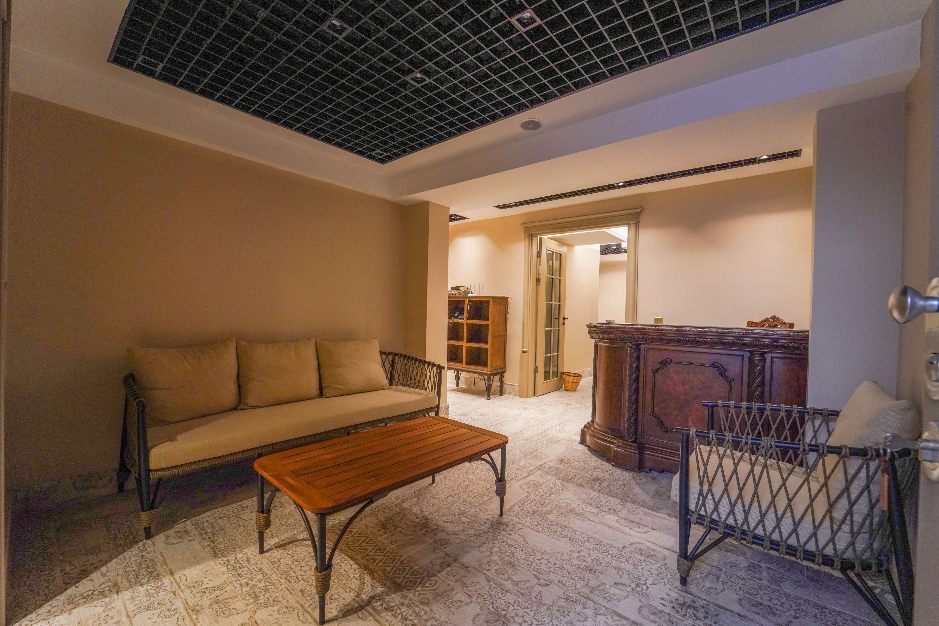 A living room with a sofa, a wooden coffee table, a baby crib, a cabinet, and a patterned rug.