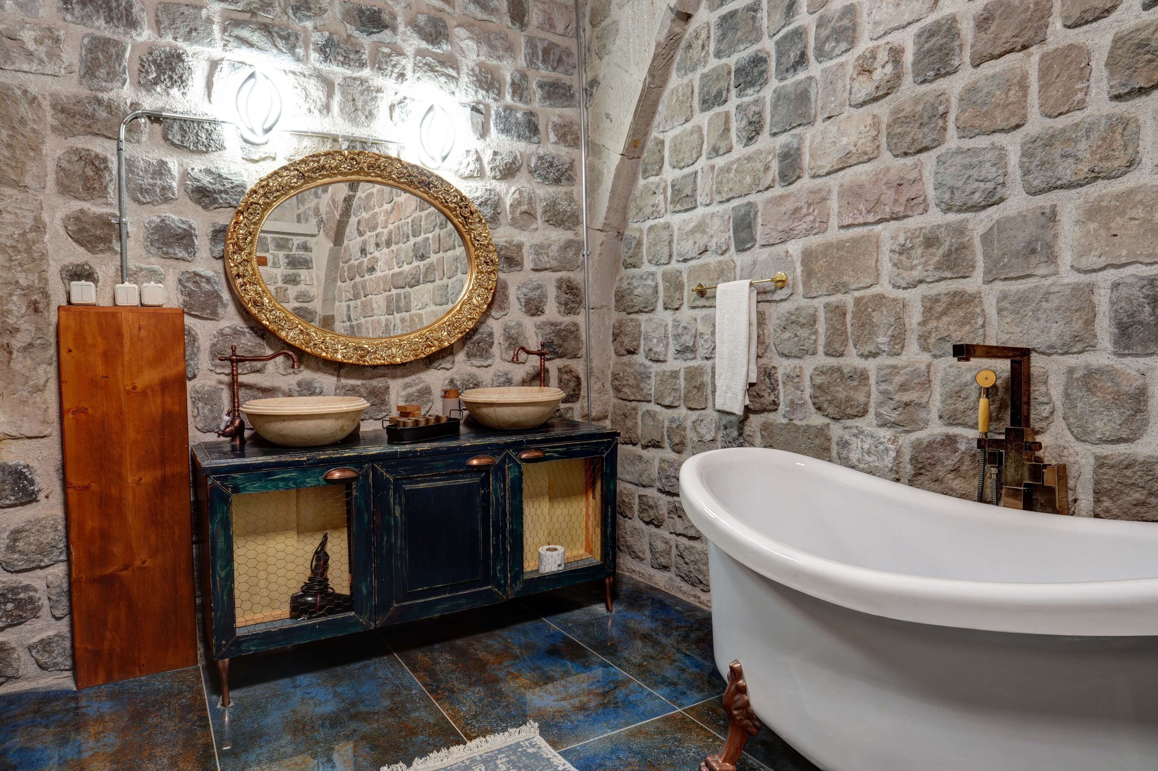 Un baño con pared de piedra, tocador de madera con dos lavamanos, un espejo grande y una bañera independiente.