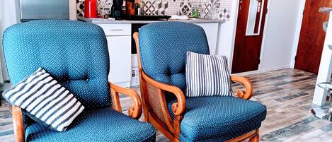 A kitchen with a microwave and refrigerator, two blue patterned chairs with cushions, and a patterned backsplash.