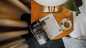 Una revista sobre una mesa de madera con una taza de café y una planta.