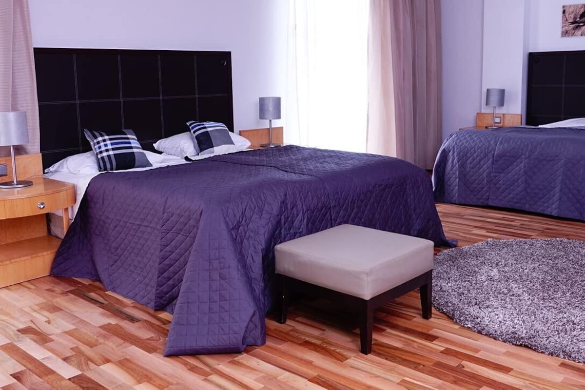 A hotel room with two beds, a bench, and a small rug.