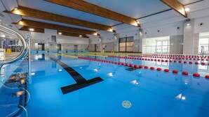 Una piscina interior con suelo azul, vigas de madera en el techo y un puesto de socorrista a la izquierda.