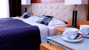 Habitación de hotel con una cama grande, dos mesitas de noche, dos lámparas y una mesita con tazas y un libro.