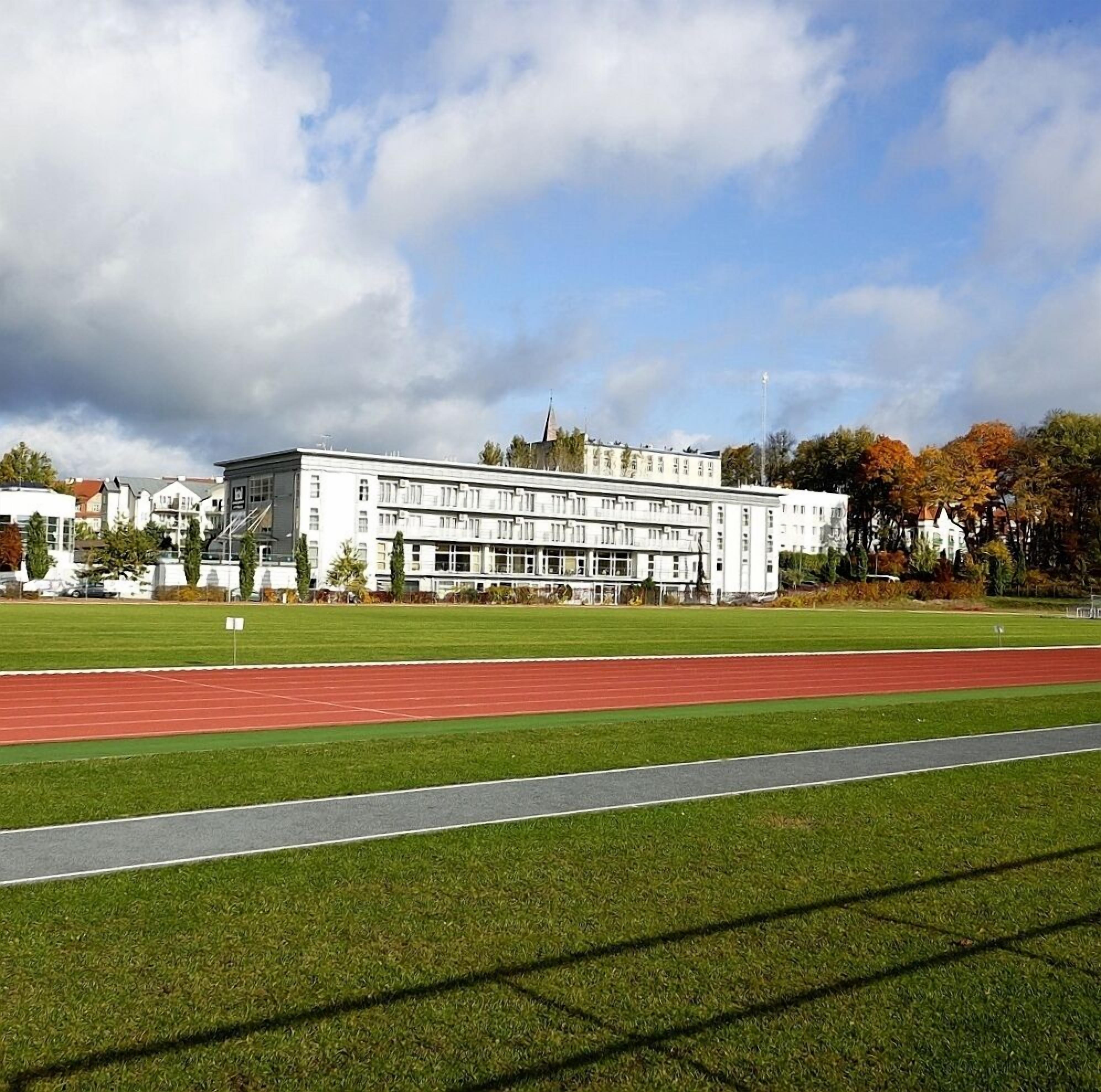 A large building with multiple floors, surrounded by a green field and a running track.