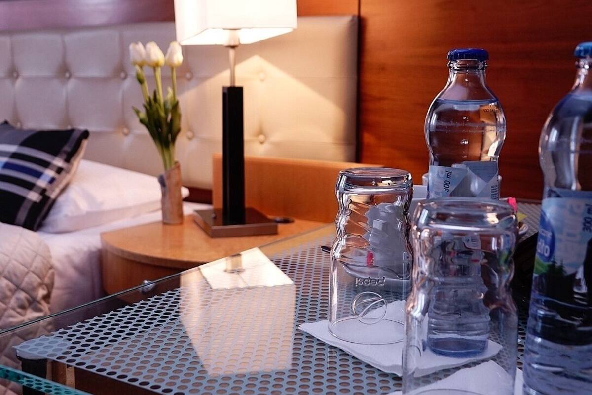 A hotel room with a neatly arranged table featuring a glass water bottle, a clear glass, and a white rectangular object.