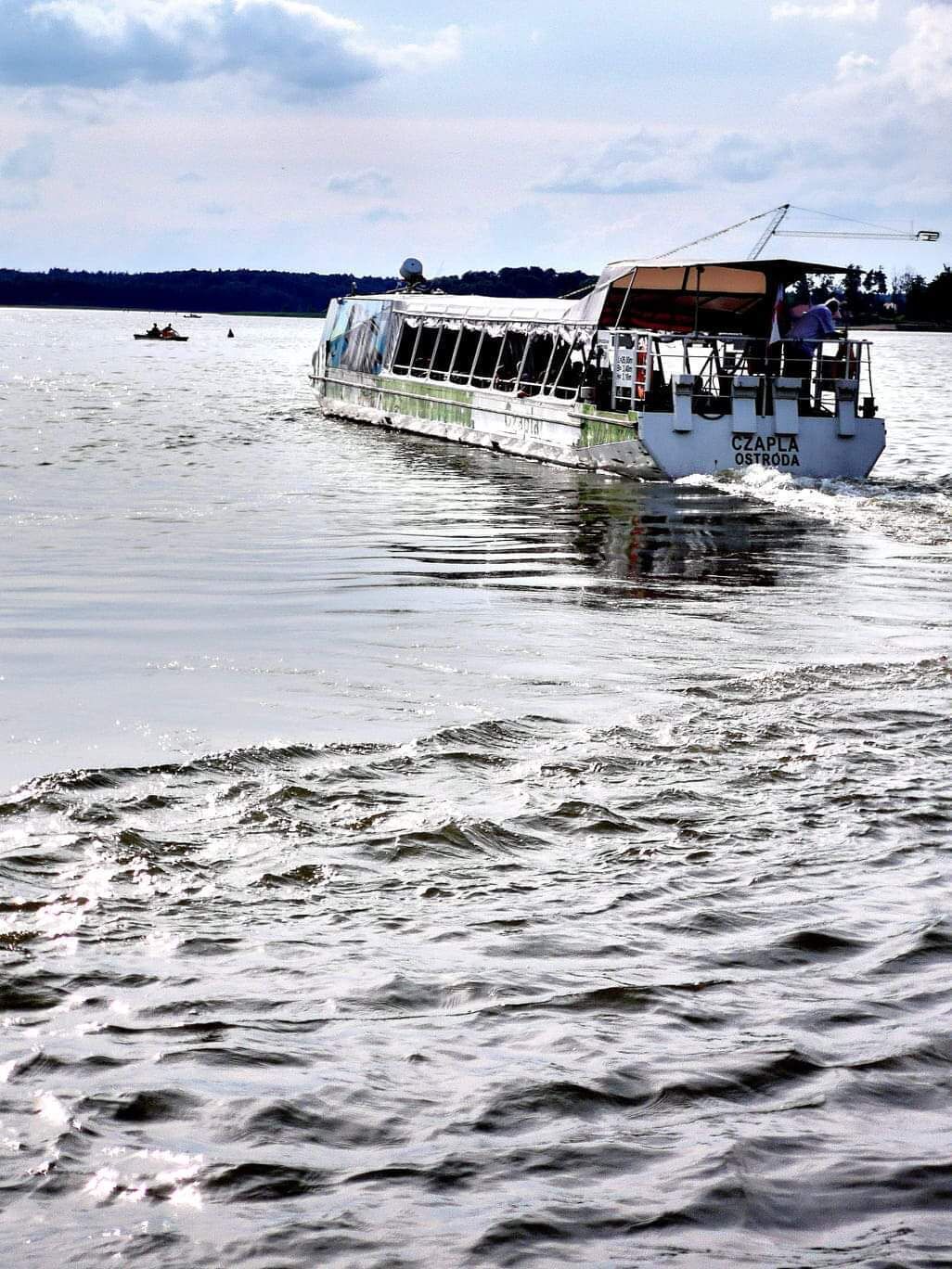 Un bateau portant le nom « CZAPLA OSTRODA » sur sa coque, naviguant sur une étendue d’eau.
