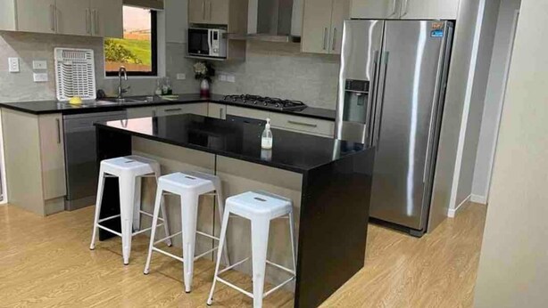 A modern kitchen with a central island, stainless steel appliances, and white bar stools. - Beautiful 1 bedroom house (Auckland)