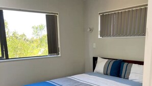 A bedroom with a bed, a window with curtains, and a view of greenery outside. - Beautiful 1 bedroom house (Auckland)