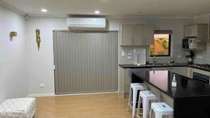 A modern kitchen with a central island, white bar stools, and a window providing natural light. - Beautiful 1 bedroom house (Auckland)