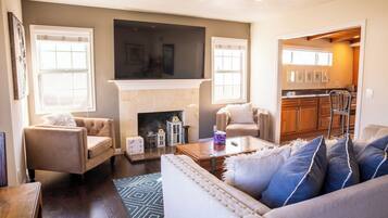 A living room with a fireplace, a television, and a kitchen visible through an open doorway.