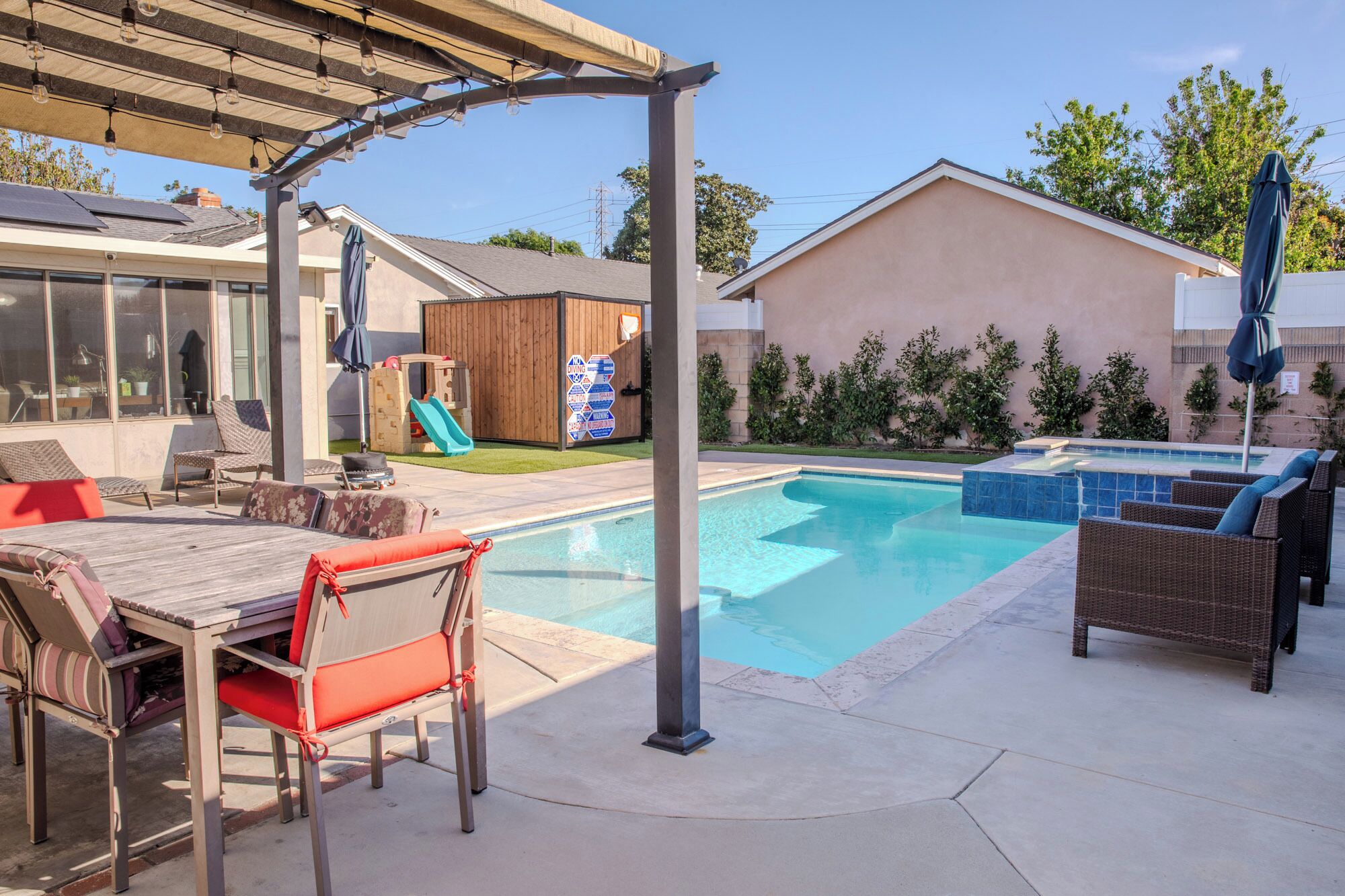 A backyard with a swimming pool, outdoor furniture, a pergola with string lights, and a slide.