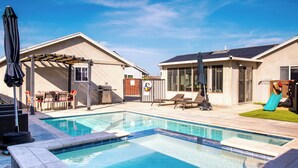 Un jardin avec une piscine, des chaises longues, un barbecue et un toboggan.