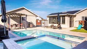 A backyard with a swimming pool, lounge chairs, a barbecue, and a slide.