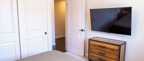 A bedroom with a bed, a dresser, a TV mounted on the wall, and a closet with two doors.