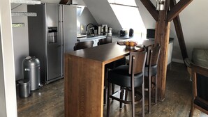 A compact kitchen with a wooden table and chairs, a refrigerator, and a sink. - Penthouse 1872 (Bayreuth)