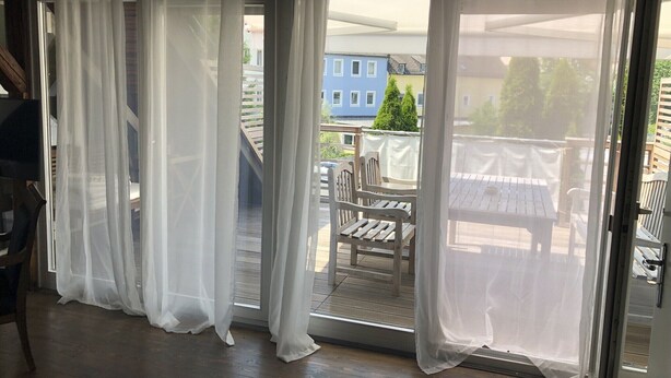 A room with a sliding glass door leading to an outdoor balcony with a wooden table and chairs. - Penthouse 1872 (Bayreuth)