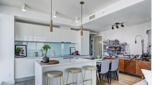 A modern kitchen with white cabinets, a central island with stools, pendant lighting, and a cityscape mural.