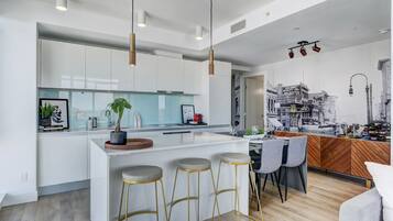 A modern kitchen with white cabinets, a central island with stools, pendant lighting, and a cityscape mural.