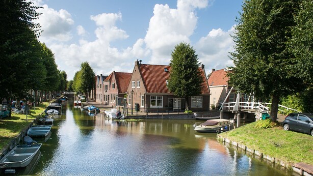 A canal with boats docked on the left, a bridge in the middle, and buildings with red roofs on the right. - Cosy chalet in the heart of Monnickendam with terrace (Monnickendam)