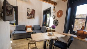 A cozy living room with a sofa, a dining table, and a large window. - Cosy chalet in the heart of Monnickendam with terrace (Monnickendam)