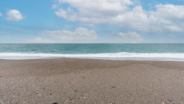 Una playa de guijarros con vista al océano bajo un cielo parcialmente nublado.