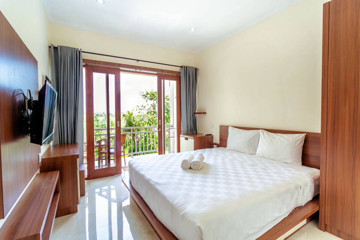 A hotel room with a large bed, wooden furniture, a TV, and a balcony with curtains.