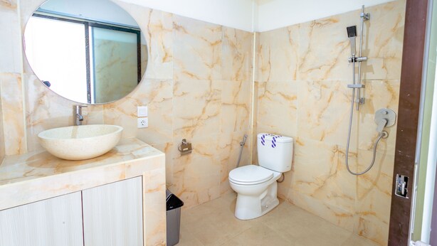 A bathroom with a marble vanity, a round mirror, a toilet, and a shower. - Sedana Cottage (Pererenan)