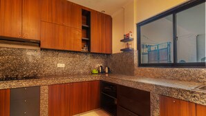 A kitchen with wooden cabinets, granite countertops, and a window with a view of a house. - Sedana Cottage (Pererenan)