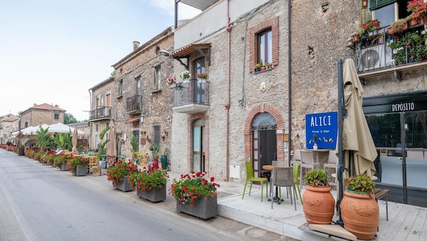 Una fila di edifici in pietra con balconi, posti a sedere all'aperto e fioriere lungo la strada.