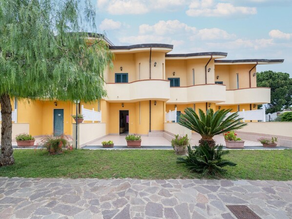 Ein mehrgeschossiges Gebäude mit gelber Fassade, einem Pflastervorplatz und Blumentöpfen.