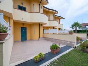 Ein mehrstöckiges Wohngebäude mit einer geschwungenen Fassade, einer grünen Tür und einer gefliesten Terrasse mit Topfpflanzen.