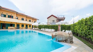 A swimming pool with lounge chairs, a stone sculpture, and a building with balconies in the background.