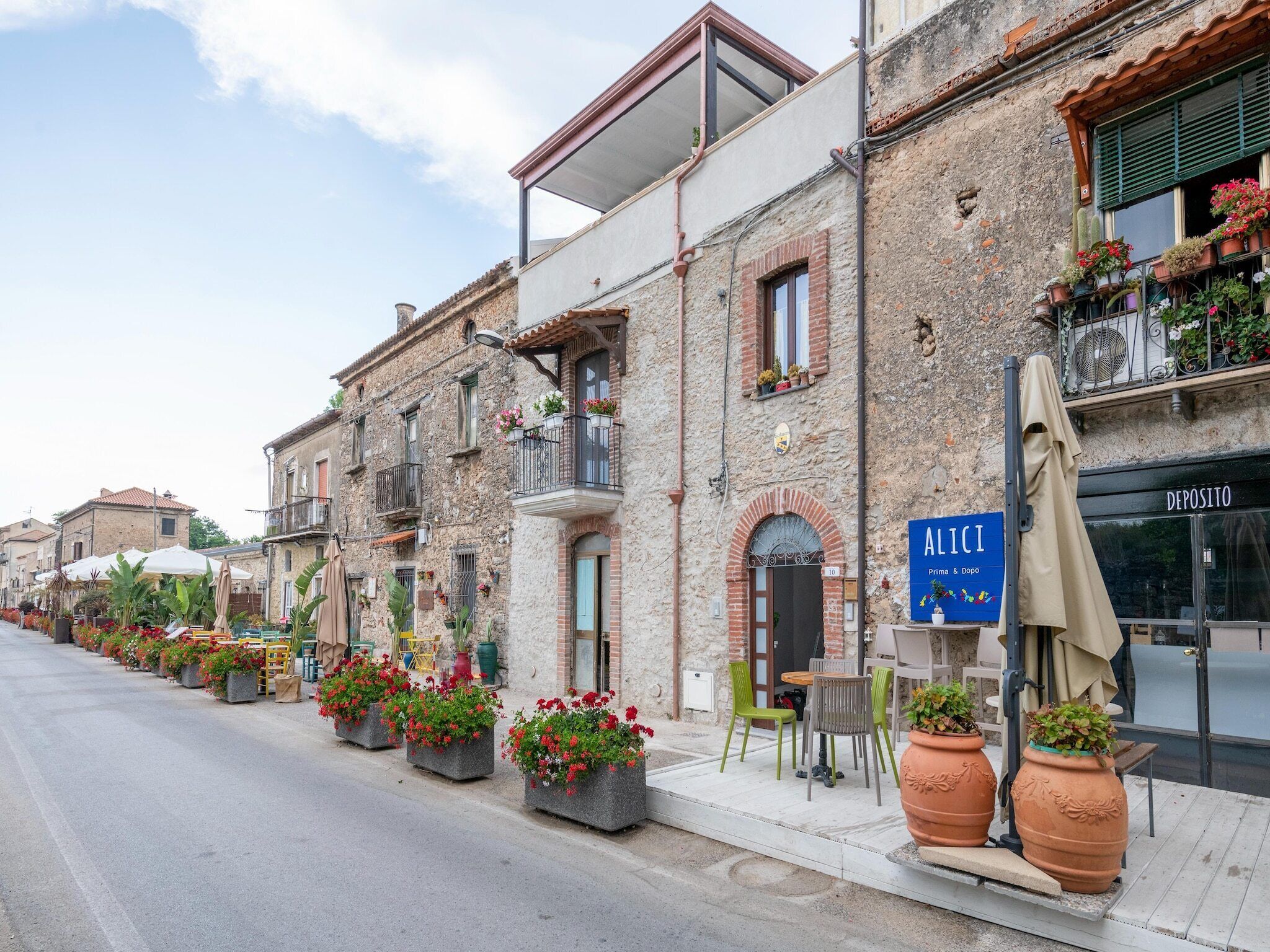 Une rangée de bâtiments en pierre dotés de balcons, de places assises en plein air et de plantes en pot.