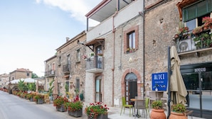 A row of stone buildings with balconies, outdoor seating, and potted plants.
