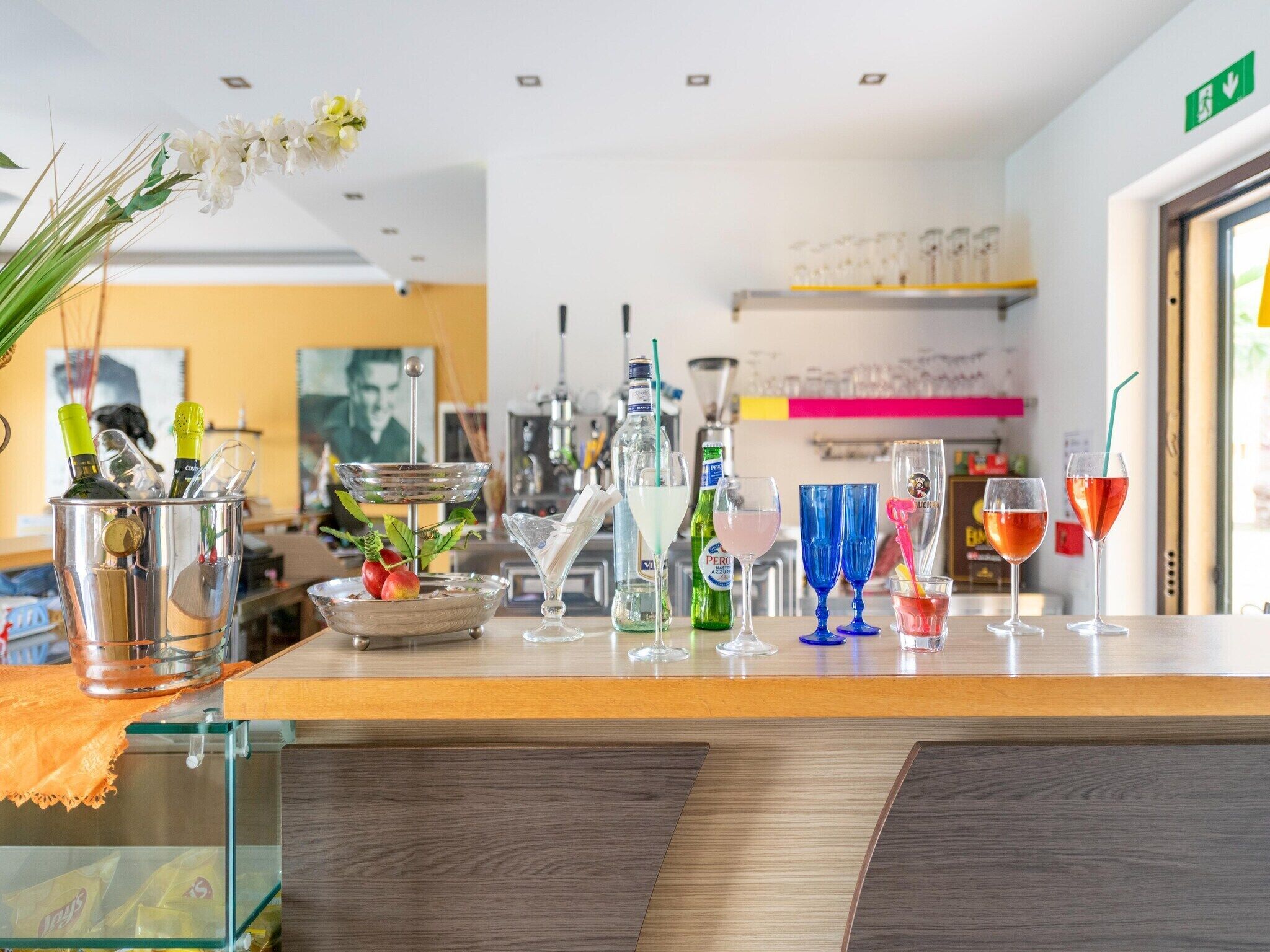 Eine Bar mit verschiedenen Flaschen und Gläsern, einem grünen Hinweisschild für den Notausgang und einer Holztheke.
