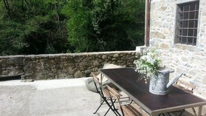 Un patio al aire libre con un muro de piedra, una mesa de madera y sillas.