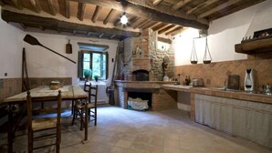 Una cocina rústica con vigas de madera a la vista, chimenea de piedra y suelo de baldosas.