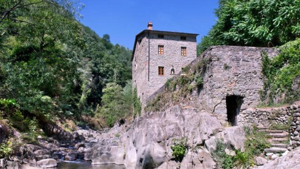 Un edificio de piedra con una ventana pequeña, rodeado por un paisaje rocoso y un río.