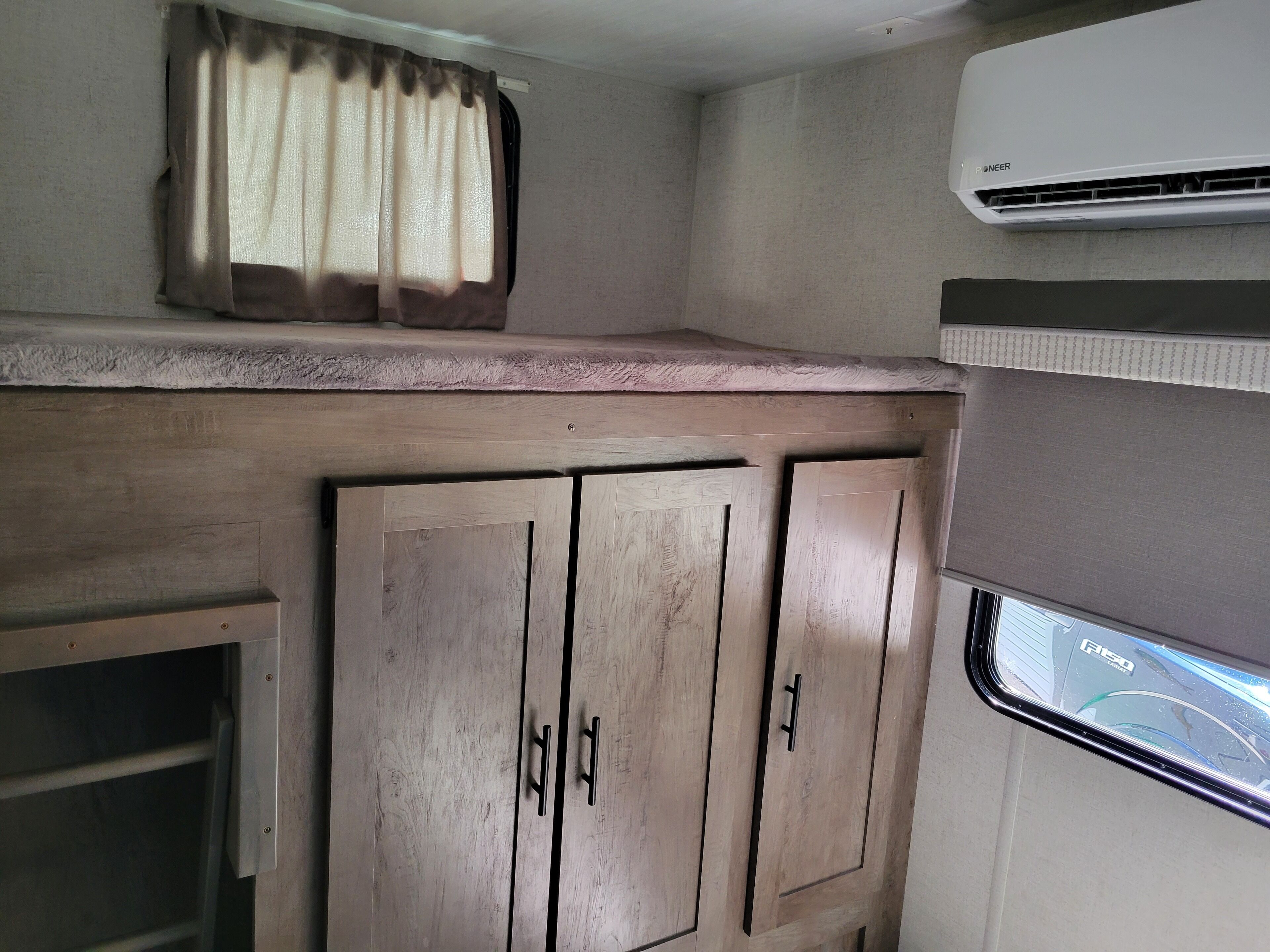 A compact RV interior with a kitchenette, including wooden cabinets and a window with a view of the road.