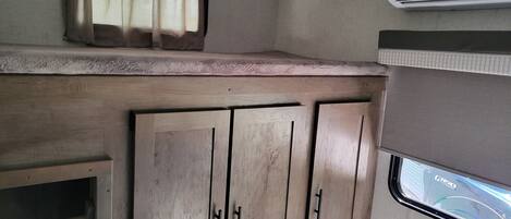 A compact RV interior with a kitchenette, including wooden cabinets and a window with a view of the road.