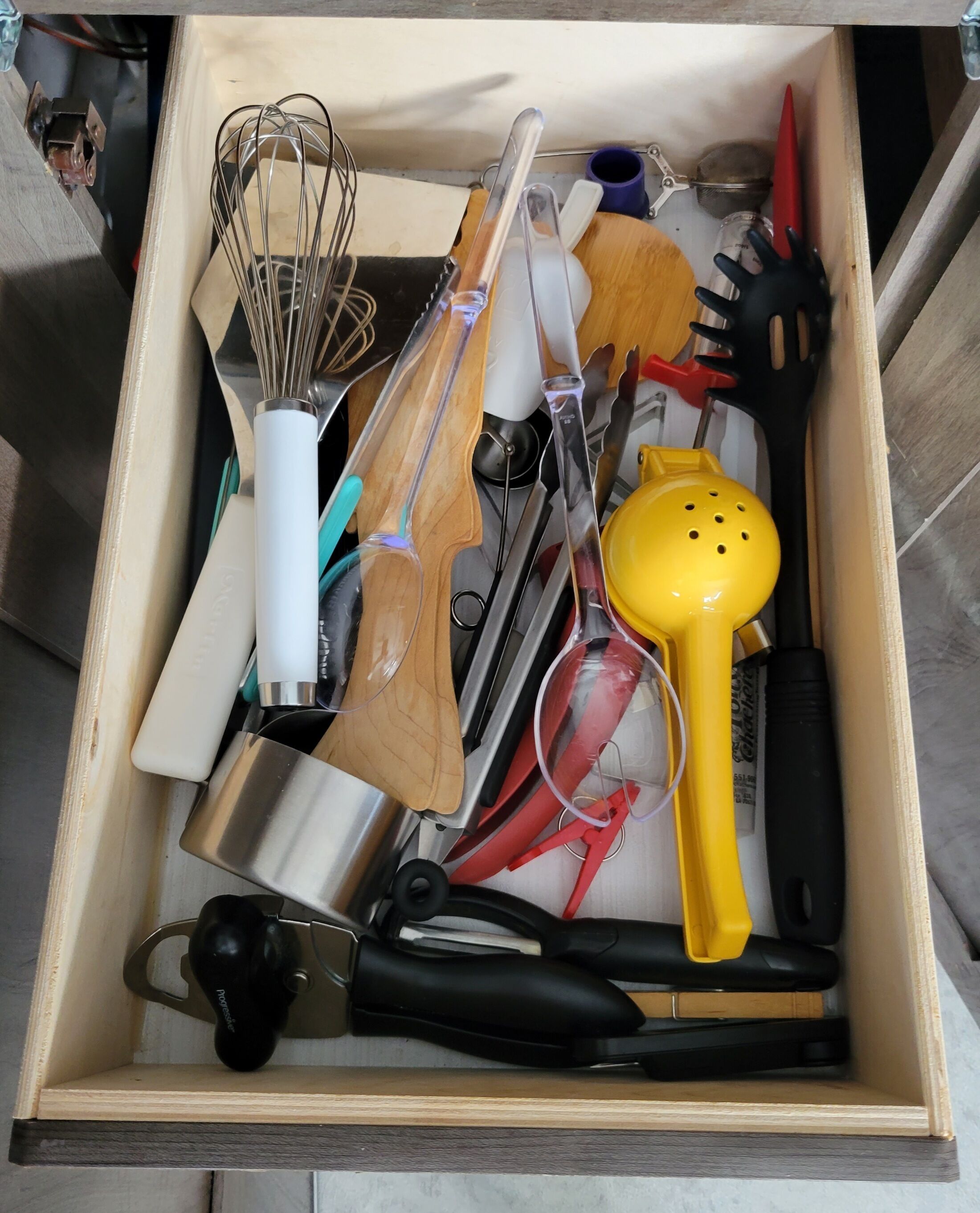A drawer containing various kitchen utensils including a whisk, spatula, and a yellow kitchen tool.