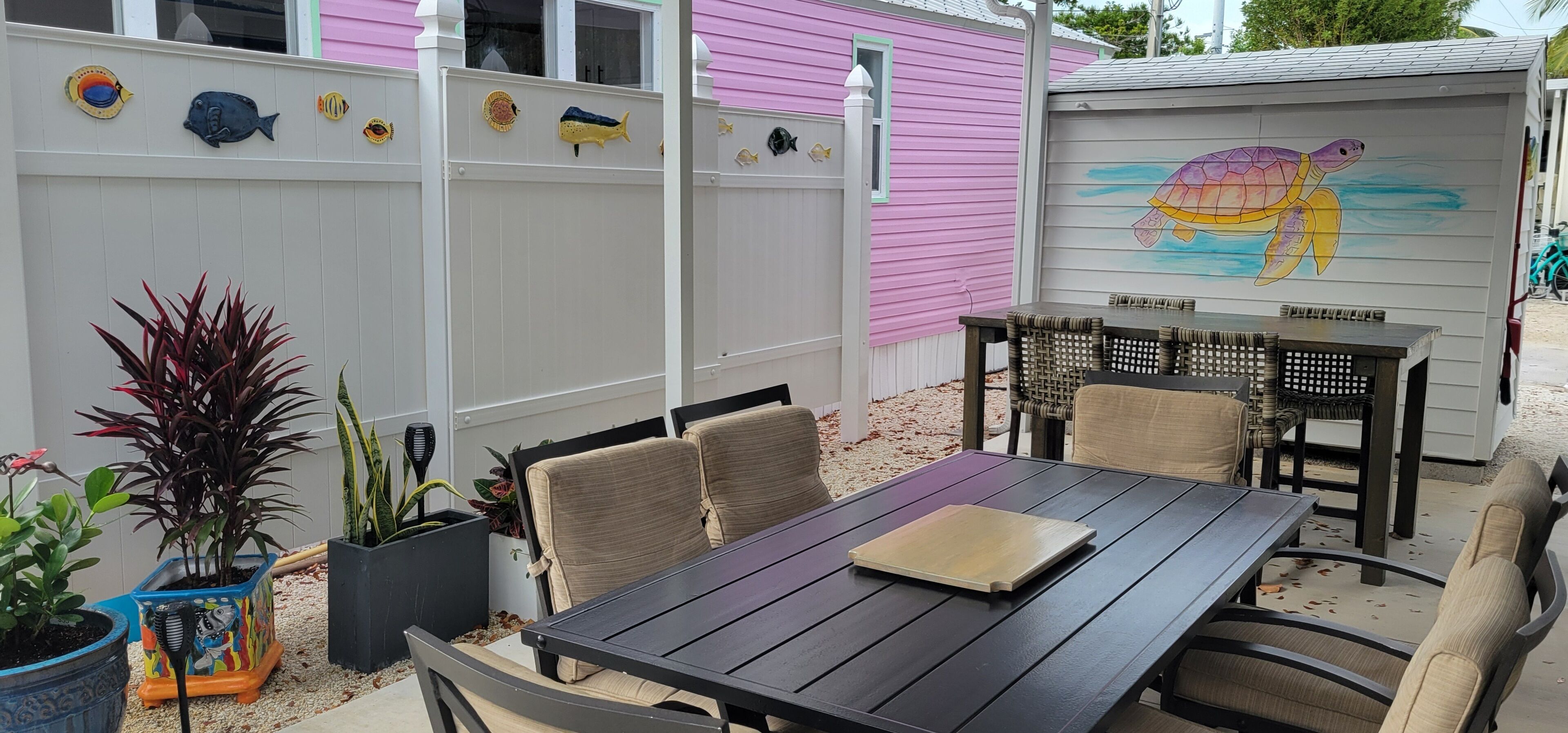 Un patio con tavolo e sedie in legno, circondato da un recinto bianco con decorazioni a forma di pesce.