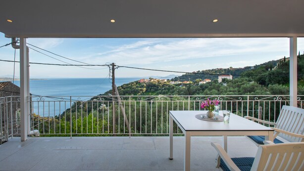 A balcony with a table and chairs, overlooking a coastal landscape with hills and a view of the sea. - Studio with breathtaking views of the sea (Corfu)