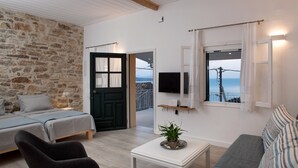 A cozy room with a bed, a sofa, a coffee table with a plant, a TV, and a view of the sea. - Studio with breathtaking views of the sea (Corfu)
