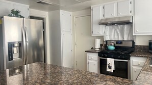 A kitchen with white cabinets, a stainless steel refrigerator, a gas stove, and granite countertops. - One story 3 bedroom home-10 minutes to strip (Las Vegas)