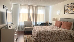 A hotel room with a bed, a desk, a chair, a window with curtains, and a painting on the wall. - One story 3 bedroom home-10 minutes to strip (Las Vegas)