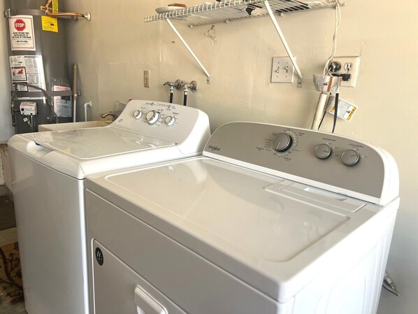 A front view of a front-loading washer and dryer unit with control knobs, a water heater, and a stop sign on the wall. - One story 3 bedroom home-10 minutes to strip (Las Vegas)