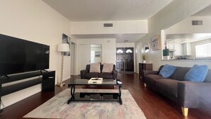 A living room with a flat-screen TV, a coffee table, two sofas, and a kitchen in the background. - One story 3 bedroom home-10 minutes to strip (Las Vegas)