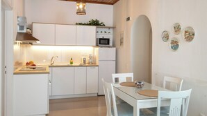 A modern kitchen with white cabinets, a microwave, and a coffee maker. There is a dining table with white chairs and a small rug. - Two bedroom apartment with breathtaking views (Corfu)